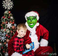 a young boy sitting next to a man dressed as the grinch and christmas tree