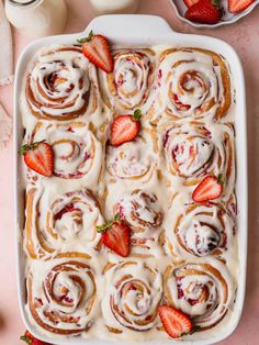 strawberry rolls with icing and strawberries in a white dish on a pink surface