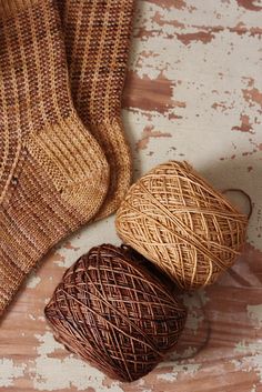 two balls of yarn sitting on top of a wooden floor next to a pair of brown socks