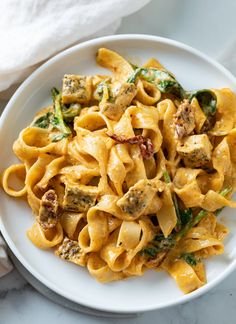 a white plate topped with pasta covered in chicken and spinach sauce on top of a marble counter