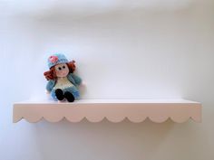 a stuffed doll sitting on top of a shelf with scalloped edges and a blue knitted hat