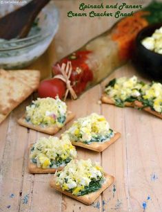 small crackers with spinach and cheese on them sitting on a wooden table next to vegetables