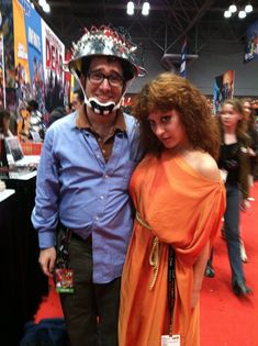 a man and woman dressed up in costumes at a convention or show, posing for the camera