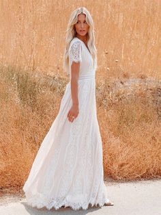 a woman in a long white dress standing on the side of a road near tall grass