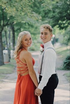 two people standing next to each other holding hands and smiling at the camera with trees in the background