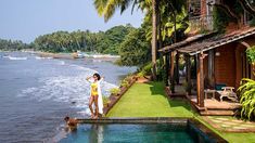 a woman standing on the edge of a swimming pool next to a lush green beach