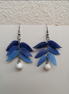 two pairs of earrings with blue leaves and pearls hanging from chains on a white surface