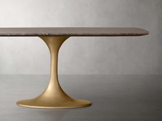 an oval table with a gold base and marble top, against a gray wall background