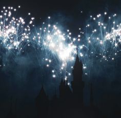 fireworks are lit up in the night sky over a castle with towers and spires