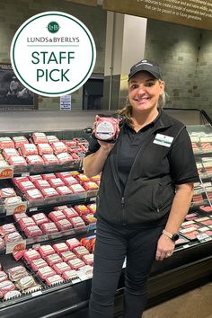 a woman standing in front of a display case holding up a piece of meat with the words staff pick on it