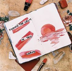 an open notebook with writing on it and various other items surrounding it, including lipstick