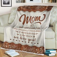 a blanket with the words mom on it sitting in front of a white chair next to a bookshelf