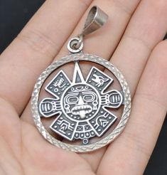 a hand holding a silver pendant with an image of a sun god in the center