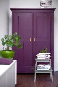 a purple cabinet in the corner of a room with a potted plant next to it