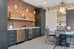 a kitchen with brick walls and grey cabinets, an island table and chairs in the center