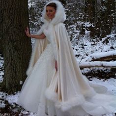 a woman in a wedding dress standing next to a tree wearing a white fur stole