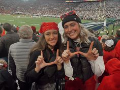 two women standing in the middle of a football stadium holding up peace signs with their hands