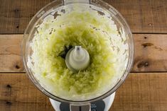 a food processor filled with green vegetables on top of a wooden table