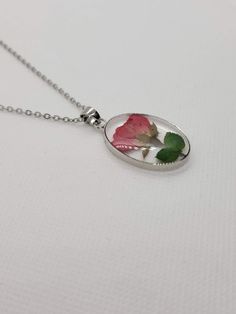 a necklace with a rose in it on a white tablecloth and a silver ball chain