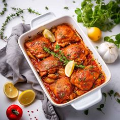 a casserole dish with chicken, lemons and parsley on the side