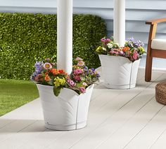 three white planters filled with colorful flowers on a porch