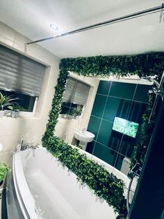 White curved bath with a large mirror above made out of small IKEA sticky back mirrors. Mirror surrounded by fake foliage around all four edges. Artificial Grass Wall With Mirror, Artificial Grass Wall Bathroom, Fake Green Wall Bathroom, Fake Foliage Wall, Fake Plant Wall Bathroom, Grass Wall Bathroom Ideas, Grass Wall With Mirror, Grass Wall In Bathroom, Mirror Plant Wall