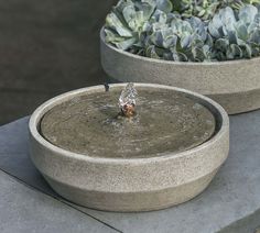 two cement bowls with plants in them and one has a water fountain on the outside