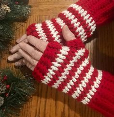 someone is holding their hand out in front of the christmas tree and wearing a red and white knitted mitt