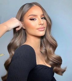 a woman with long, wavy hair is wearing a black top and has her hand on her head