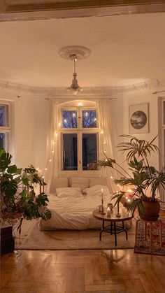 a bed room with a neatly made bed surrounded by potted plants and candles on the floor