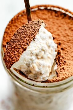 a glass filled with chocolate pudding and cream on top of a white table next to a spoon