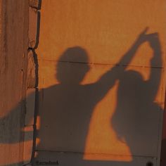 a shadow of a person holding a skateboard in front of a wall with an orange background