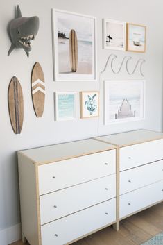 a white dresser sitting next to a wall filled with pictures and surfboards on top of it