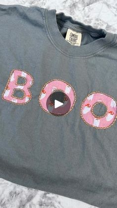 a gray shirt with pink donuts on it and the word boo spelled out in large letters