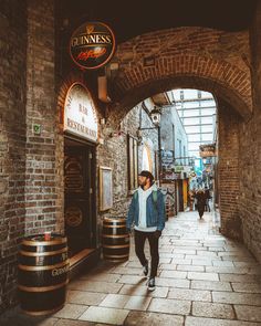 a man is walking down the street in an alley way with barrels on either side