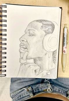 a pencil drawing of a man with headphones on his ears, next to a notebook and pen