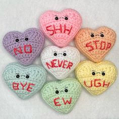 six crocheted hearts with faces and words written on them, all in different colors