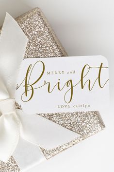 a white and gold christmas card with a bow on it's side that says merry and bright