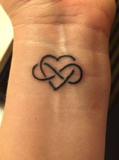 a black tattoo on the wrist of a woman with two intertwined hearts in it