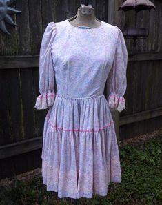 This sweet vintage dress was most likely made in the 70s, but has decidedly 50s styling. This 70s dress was hand sewn by Katherine Dean as a square dancing dress. The fabric feels like cotton and comes in delicate floral print. Colors are pale pink, lavender, gold, sage green and white. Sleeves are puffed and trimmed in creamy lace and pink velvet ribbon. Pleated circle skirt is also trimmed in pink velvet and creamy lace. If you aren't using this beautiful dress for square dancing, it also make Vintage Knee-length Fitted Prairie Dress, Vintage Fitted Knee-length Prairie Dress, Retro Long Sleeve Prairie Dress, Vintage Fitted Prairie Dress For Vintage Fashion, Fitted Vintage Prairie Dress For Vintage Fashion, Vintage Knee-length Prairie Dress For Spring, Fitted 1970s Vintage Dress, Spring Vintage Knee-length Prairie Dress, Fitted Vintage Prairie Dress