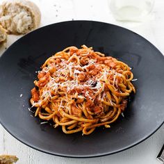 a black plate topped with pasta covered in sauce and parmesan cheese next to bread