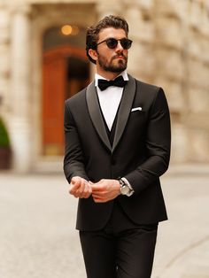 a man in a tuxedo is walking down the street with his hand on his hip