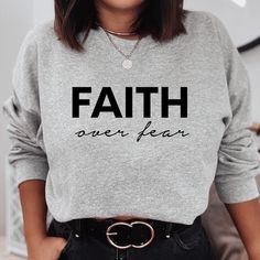 Keep warm and comfortable in this Faith Over Fear Sweatshirt. This cool Christian sweatshirt is soft, stylish, and sure to keep you warm in the colder months. It's versatile to wear for a day outdoors, heading to the gym, or a lazy day watching movies on the couch. Wearing Christian hoodies and sweatshirts can be a subtle way to express your faith and create conversations with anyone and be a gentle reminder to encourage you in any season. They can also spread encouraging words of faith everywhe Winter Gray Letter Print T-shirt, Cozy Gray Tops With Letter Print, Cozy Gray Top With Letter Print, Cozy Gray Letter Print Top, Gray Winter Loungewear T-shirt, Fall Slogan Tops For Leisure, Cozy Gray Sweatshirt With Letter Print, Winter Graphic Print Sweatshirt, Winter Graphic Print Comfortable Sweatshirt