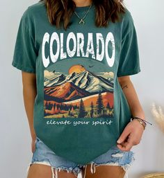 Celebrate the majestic beauty of Colorado's mountains with this striking graphic tshirt, designed for those who love hiking adventure and scenic landscapes. Featuring a captivating design that pays homage to the state's iconic peaks and wilderness, this tee is a perfect gift for anyone enchanted by Colorado's natural wonders. Whether you're hiking trails or strolling through town, this shirt is a stylish way to show your admiration for the Rockies. The Comfort Colors C1717 100% Ring Spun Cotton Green T-shirt With Letter Print For Outdoor Activities, Green Letter Print T-shirt For Outdoor Activities, Green Letter Print Tops For Hiking, Green Tops With Letter Print For Hiking, Green Graphic Tee For Outdoor Activities, Graphic Print Relaxed Fit Top For Hiking, Relaxed Fit Graphic Print Top For Hiking, Green T-shirt With Letter Print For Outdoors, Green Graphic Tee For Hiking