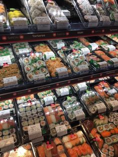 an assortment of sushi and other foods on display in a case at a grocery store