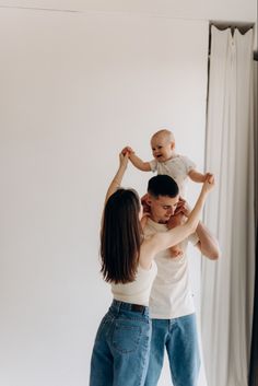 a man and woman holding a baby up in the air while standing next to each other