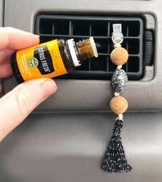 a person is holding an orange and black bottle in their hand next to a car air freshener dispenser