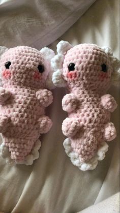 two crocheted stuffed animals laying on top of a white bed sheet, one is pink and the other is white with black eyes