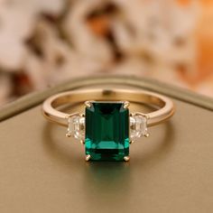 an emerald and diamond ring sitting on top of a table