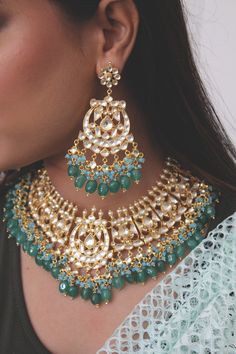 Kundan Gold Plated Indian Bridal Jewellery with Emerald Green stones and light blue agate stones, Semi precious Uncut Kundan Polki Indian Wedding Necklace with Chandbali Earring. Gold Plated kundan and uncut polki set on a silver and copper alloy base. This necklace set is plated with 22k gold and embellished with semi precious emerald green onyx stones and light blue agate stones. Heavy necklace set with chandbaali earrings for bridal dressing.This Sabyasachi inspired necklace with a twist of c Blue Fusion Style Tilla Jewelry, Blue Tilla Fusion Jewelry, Blue Fusion Tilla Jewelry, Turquoise Fusion Jewelry For Wedding, Blue Chandbali Jewelry With Cutdana Detail, Blue Chandbali Jewelry With Cutdana, Fusion Style Blue Kundan Jewelry, Turquoise Meenakari Necklace For Wedding, Blue Cutdana Chandbali Jewelry